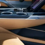 The meticulously designed center console of the Escalade IQL features premium materials with contrasting tan leather and glossy black surfaces. The console houses cup holders, storage, and control interfaces for the vehicle's numerous luxury features.