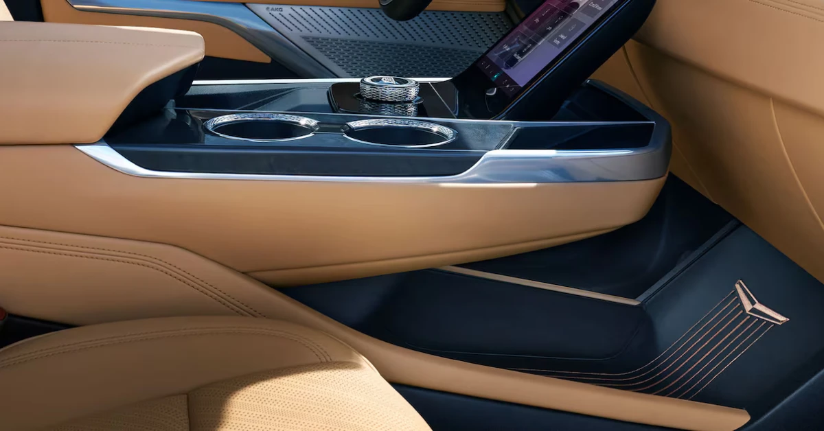 The meticulously designed center console of the Escalade IQL features premium materials with contrasting tan leather and glossy black surfaces. The console houses cup holders, storage, and control interfaces for the vehicle's numerous luxury features.