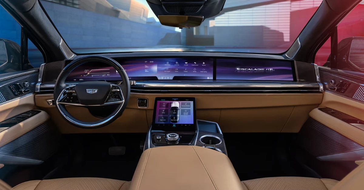 The driver's view of the 2026 Escalade IQL reveals the sweeping digital display with "ESCALADE IQL" branding and the elevated center console with climate and vehicle controls. The two-tone black and tan interior exemplifies Cadillac's premium craftsmanship.