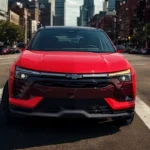 The 2025 Chevrolet Blazer EV SS displays its aggressive front fascia with illuminated black grille, slim LED headlights, and dynamic lower air intakes, captured in vibrant red against an urban backdrop.