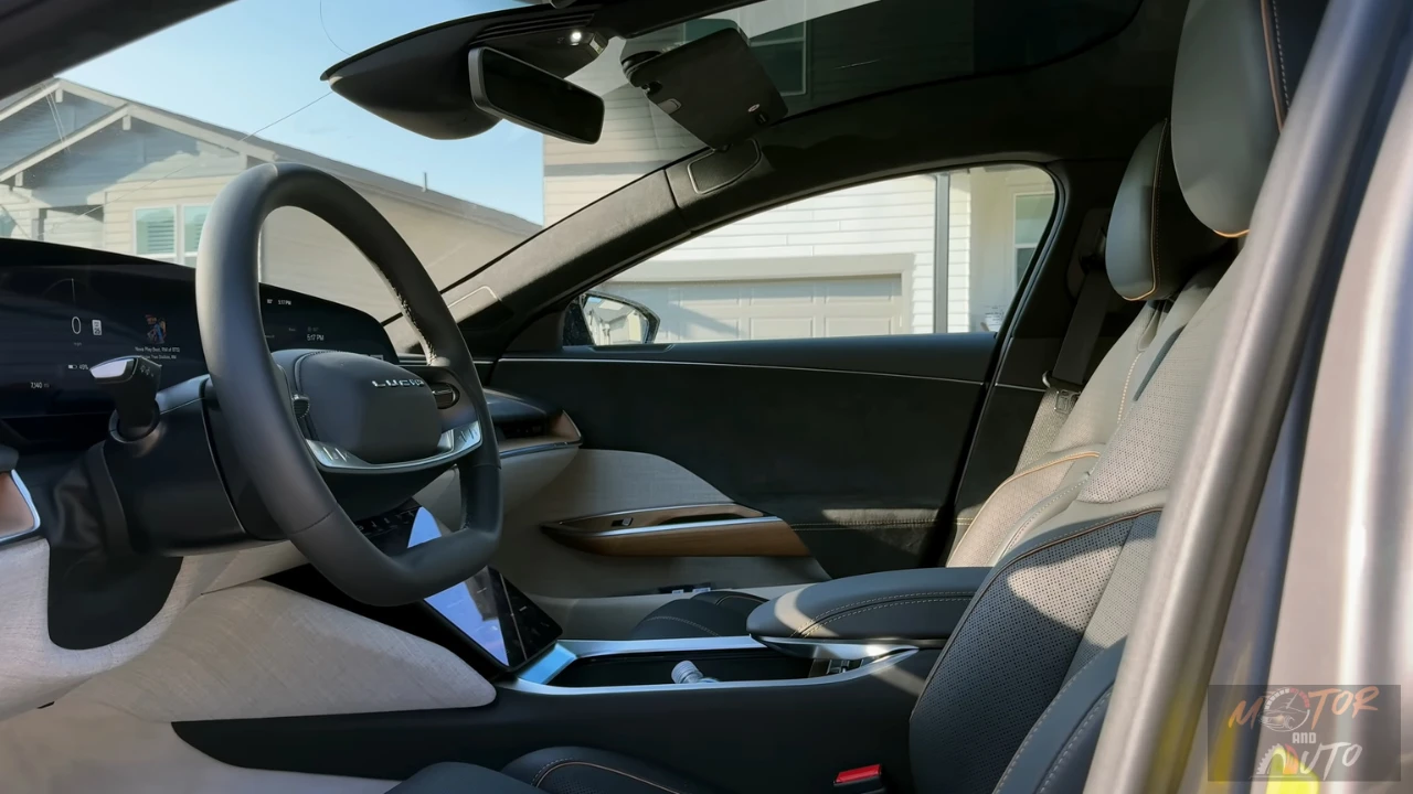Interior view of the 2025 Lucid Air driver's cockpit featuring a two-spoke steering wheel with Lucid branding, floating curved digital display, wood trim accents, and light-colored upholstery in a minimalist luxury design.