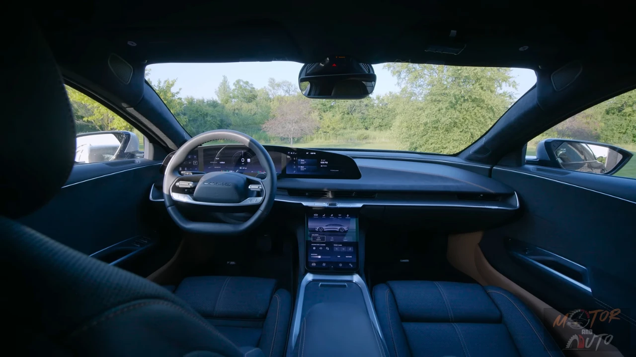Interior view from the driver's perspective of the 2025 Lucid Air showing the dark blue interior with two-spoke steering wheel, curved digital display spanning the dashboard, center touchscreen, and silver trim accents with a view of trees through the windshield.