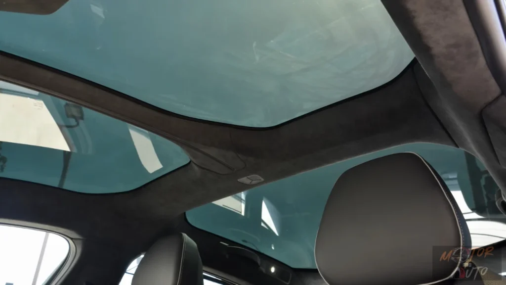 Interior view looking up at the 2025 Lucid Air's extensive glass roof panel with dark headliner material and support structure, showing a blue sky visible through the transparent roof from the interior of the vehicle.