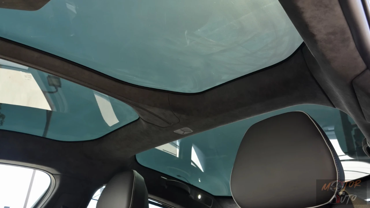 Interior view looking up at the 2025 Lucid Air's extensive glass roof panel with dark headliner material and support structure, showing a blue sky visible through the transparent roof from the interior of the vehicle.