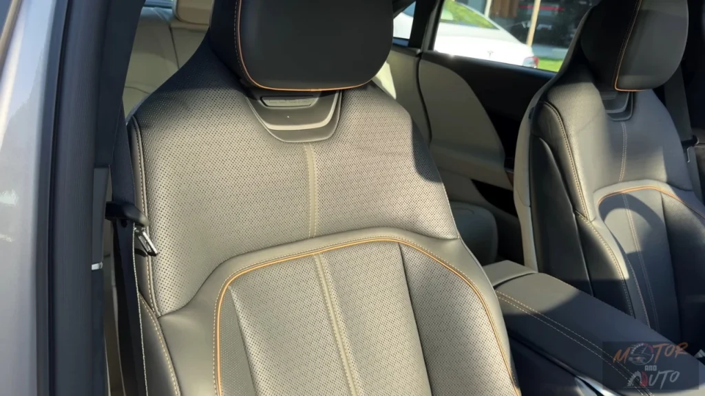 Close-up view of a 2025 Lucid Air's light gray premium front seat showing perforated leather upholstery with contrast stitching, sculpted ergonomic design, and adjustable headrest with natural light illuminating the interior.