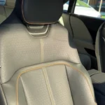 Close-up view of a 2025 Lucid Air's light gray premium front seat showing perforated leather upholstery with contrast stitching, sculpted ergonomic design, and adjustable headrest with natural light illuminating the interior.
