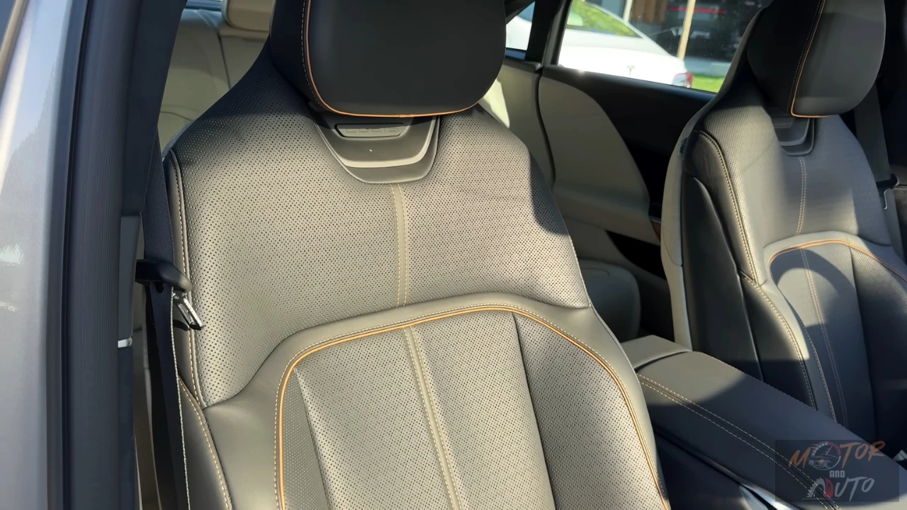 Close-up view of a 2025 Lucid Air's light gray premium front seat showing perforated leather upholstery with contrast stitching, sculpted ergonomic design, and adjustable headrest with natural light illuminating the interior.