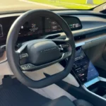 Close-up view of the 2025 Lucid Air's two-spoke steering wheel showing the Lucid branding, integrated control buttons, and digital instrument display in the background with navigation information.
