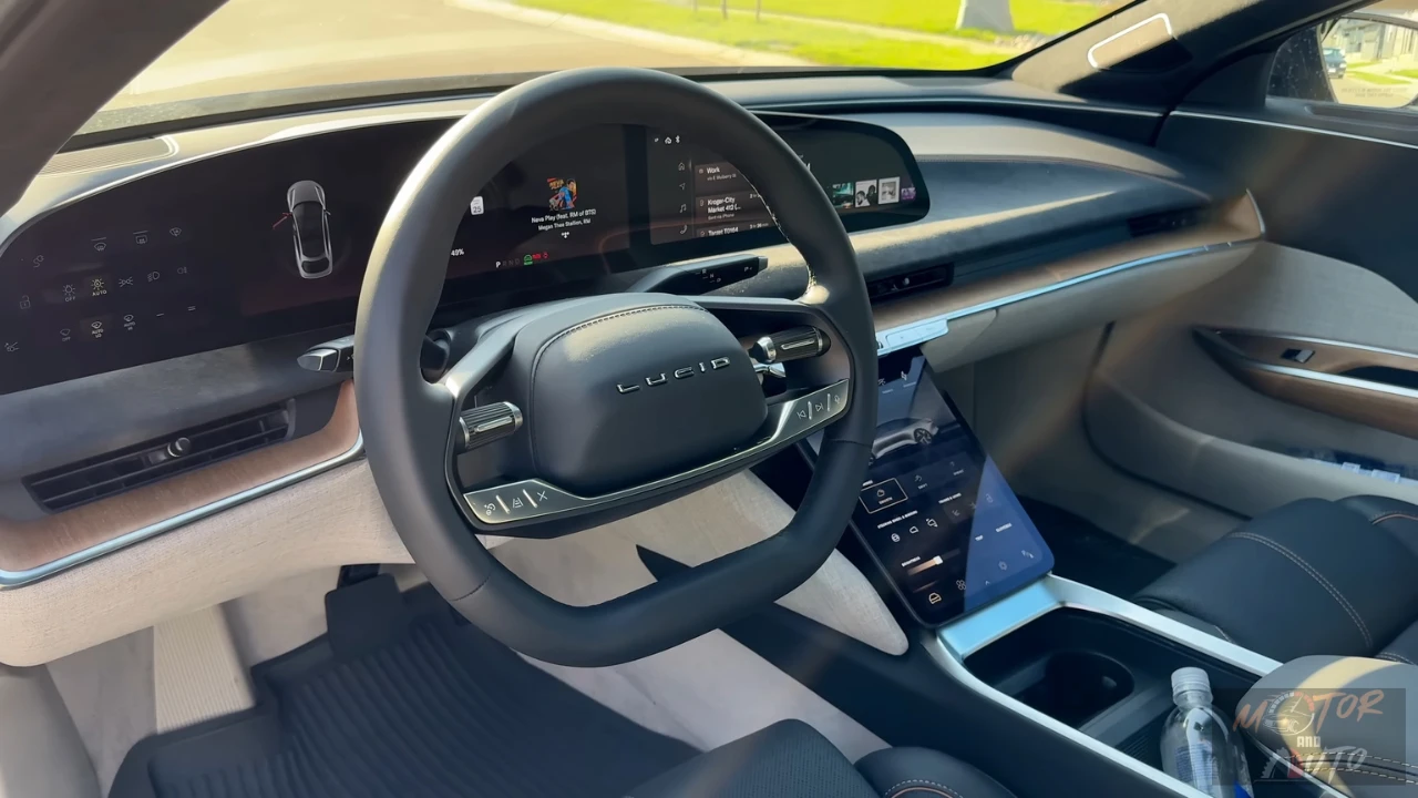 Close-up view of the 2025 Lucid Air's two-spoke steering wheel showing the Lucid branding, integrated control buttons, and digital instrument display in the background with navigation information.