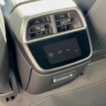 Close-up of the 2025 Lucid Air's rear center console showing climate control vents, a small touchscreen display for temperature adjustment, and silver-trimmed housing integrated into the light gray interior with premium upholstery visible.