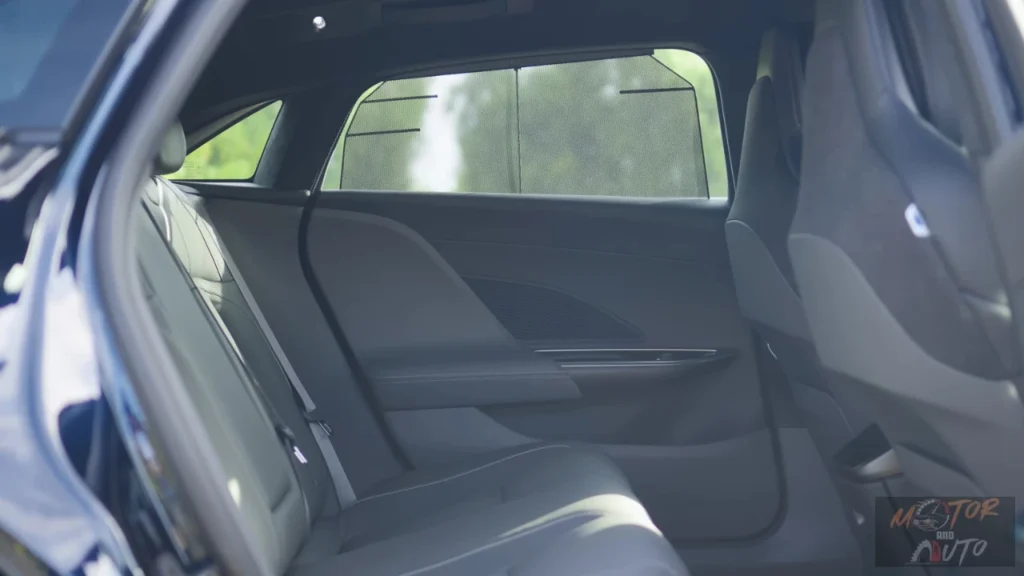 View into the 2025 Lucid Air's rear passenger compartment through an open rear door showing the expansive legroom, dark upholstered rear seats, flat floor, and rear climate control panel on the back of the center console.