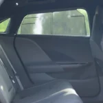 View into the 2025 Lucid Air's rear passenger compartment through an open rear door showing the expansive legroom, dark upholstered rear seats, flat floor, and rear climate control panel on the back of the center console.