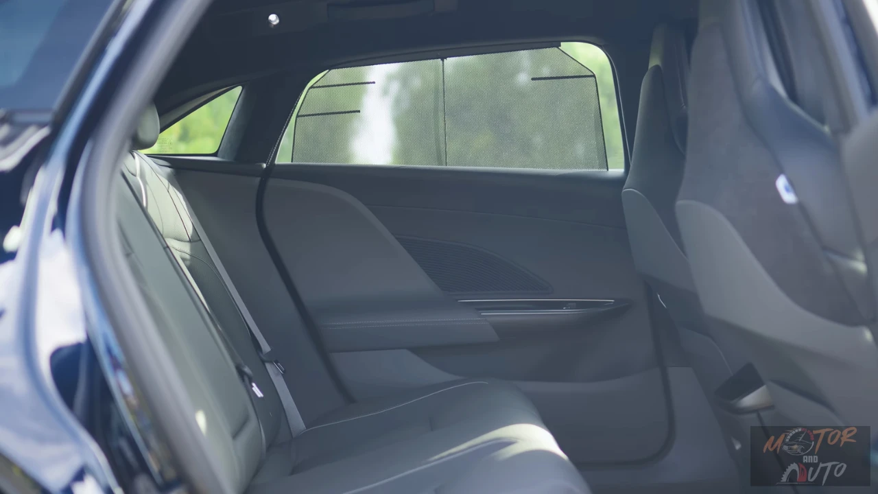 View into the 2025 Lucid Air's rear passenger compartment through an open rear door showing the expansive legroom, dark upholstered rear seats, flat floor, and rear climate control panel on the back of the center console.