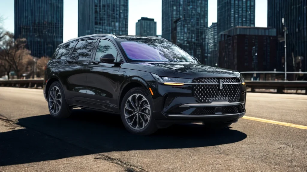 Three-quarter front angle view of 2025 Lincoln Nautilus luxury SUV in black with diamond grille, LED lighting, and premium wheel design against urban cityscape background