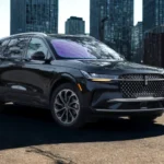Three-quarter front angle view of 2025 Lincoln Nautilus luxury SUV in black with diamond grille, LED lighting, and premium wheel design against urban cityscape background