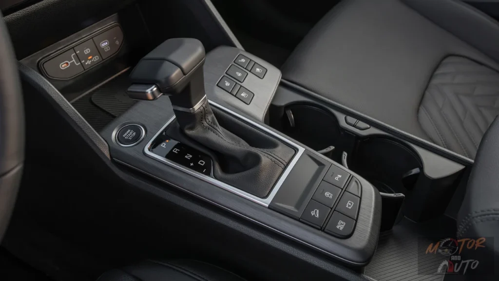 Center console of 2026 Kia Sportage showing traditional automatic gear shifter, engine start button, control buttons for heated seats, hill descent, auto hold, and parking sensors