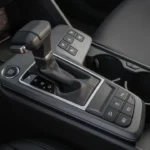 Center console of 2026 Kia Sportage showing traditional automatic gear shifter, engine start button, control buttons for heated seats, hill descent, auto hold, and parking sensors