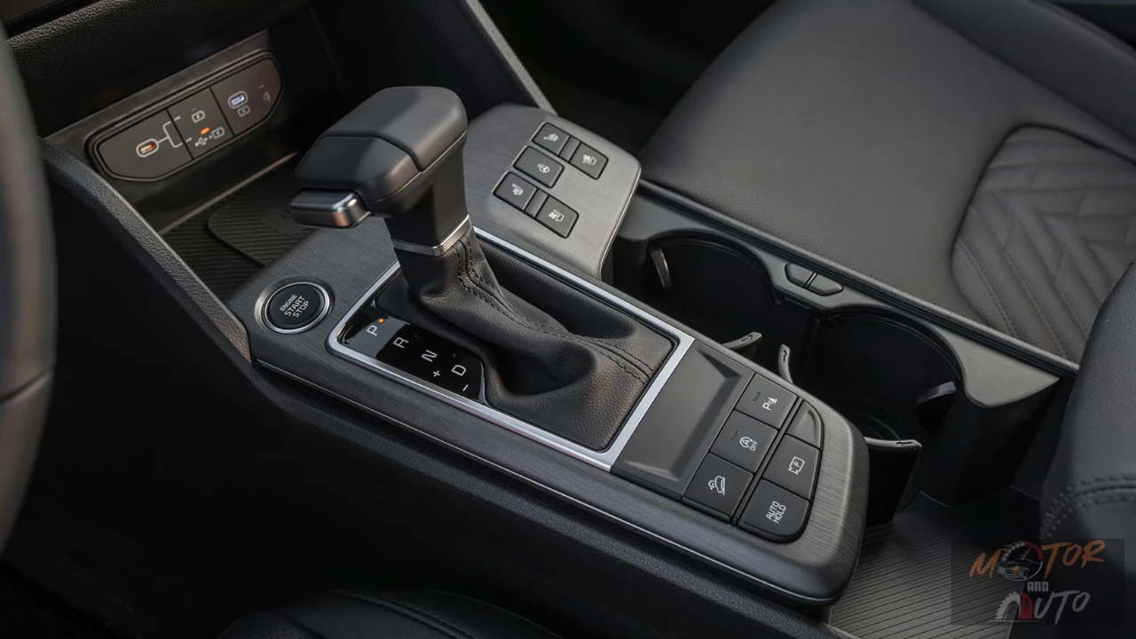 Center console of 2026 Kia Sportage showing traditional automatic gear shifter, engine start button, control buttons for heated seats, hill descent, auto hold, and parking sensors