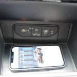 Center console of 2026 Kia Sportage showing wireless phone charging pad with smartphone and dual USB-C ports for device connectivity and charging