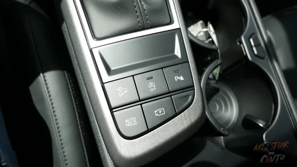 Close-up of 2026 Kia Sportage center console showing control buttons for hill descent, auto start-stop, parking assist, auto hold, and camera system activation