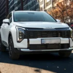 White 2026 Kia Sportage front three-quarter view on city street showing new LED headlight design, updated grille, and modern styling with urban buildings in background