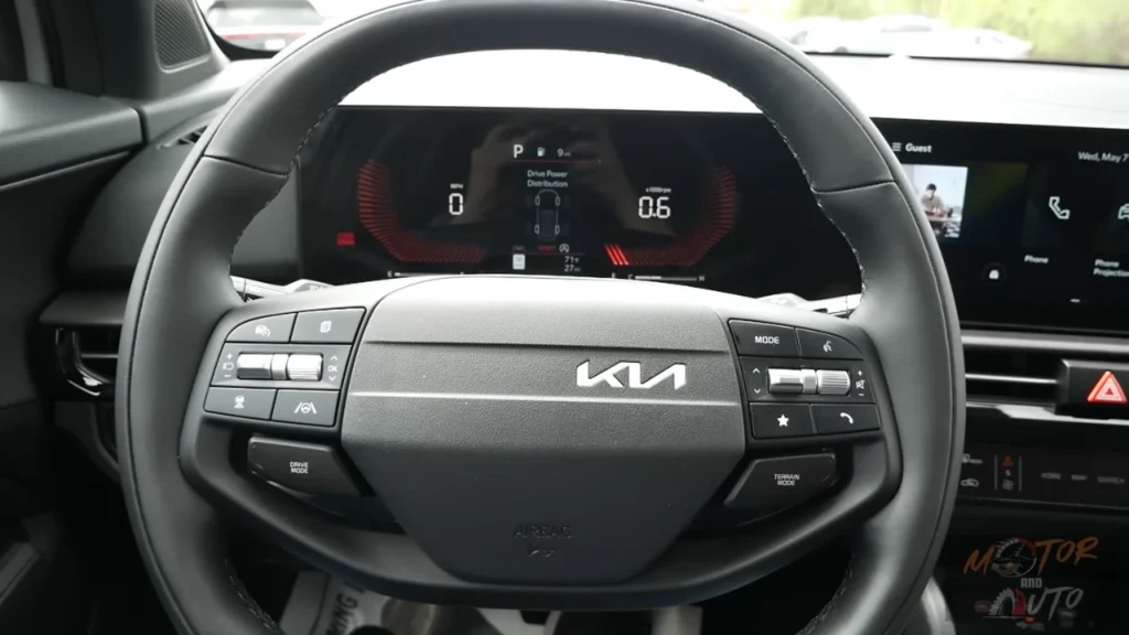 Close-up view of 2026 Kia Sportage new yoke-shaped steering wheel with physical control buttons and digital gauge cluster showing drive modes and vehicle information