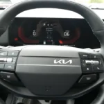 Close-up view of 2026 Kia Sportage new yoke-shaped steering wheel with physical control buttons and digital gauge cluster showing drive modes and vehicle information