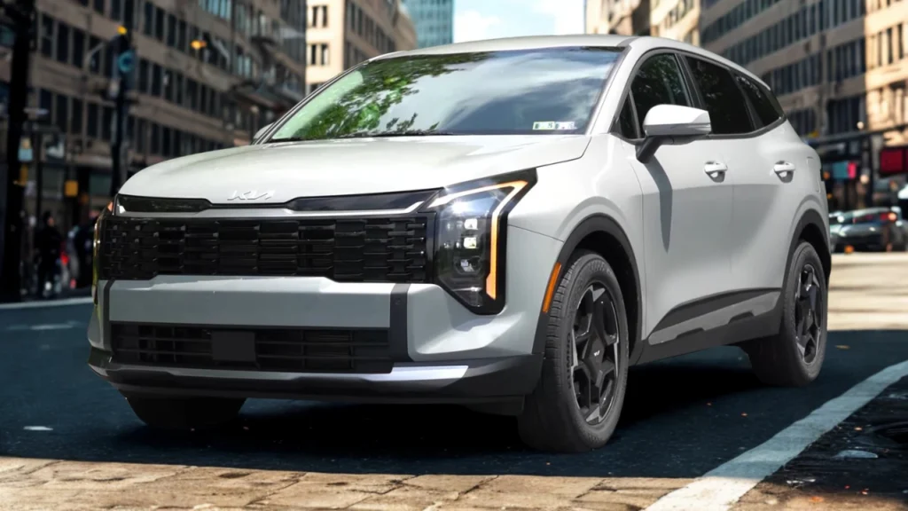 White 2026 Kia Sportage front three-quarter view with LED headlights illuminated showing amber DRL, modern front design, and urban street setting